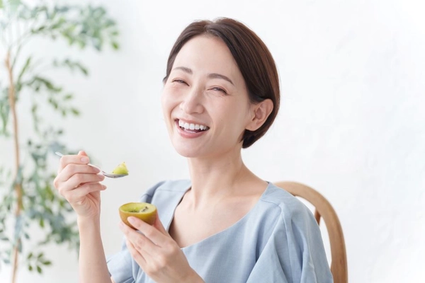 Happy woman eats gold kiwi with spoon
