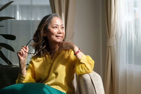 Middle aged woman resting on comfortable couch, looking away thinking dreaming enjoy stress free peaceful mood