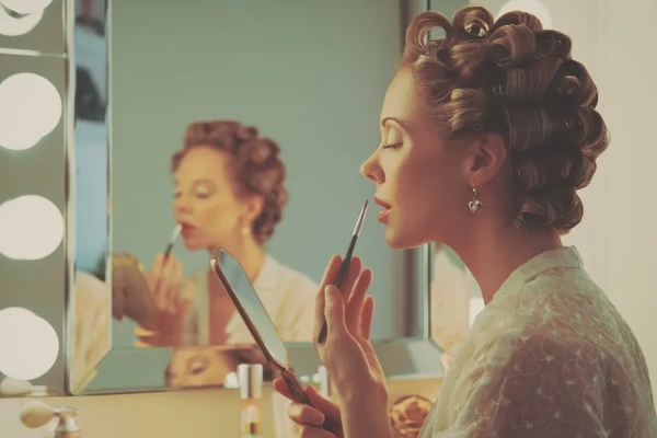Image A woman wearing curlers putting on lipstick with a lip brush.