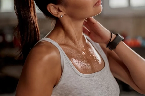 Image A woman touching her neck while she has sweat on her chest.