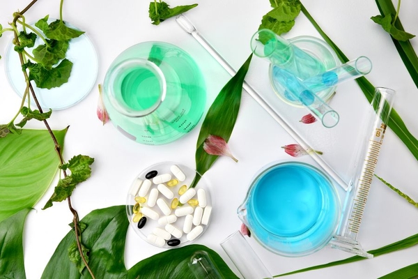 Image birds-eye photo of liquids in lab beakers and green leaves