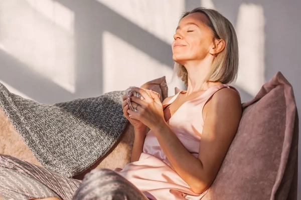 Image A woman smiling and holding a cup of tea.
