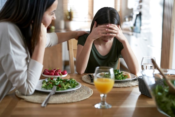 Image mother supporting her daughter at dining table, mental health and diet concept