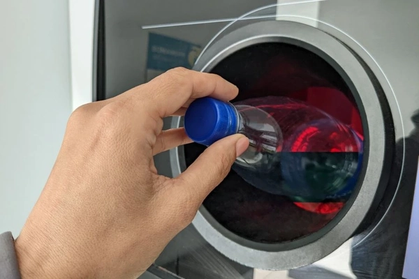 Image Man placing empty plastic bottle in reverse vending machine.