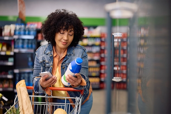 woman reading nutrition label while buying dairy product in supermarket