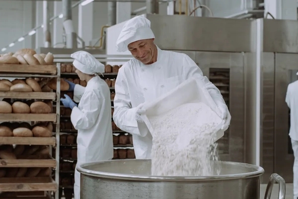 A worker pours bread baking ingredients into a large mixer in a bread factory. A worker pours bread baking ingredients into a large mixer in a bread factory.