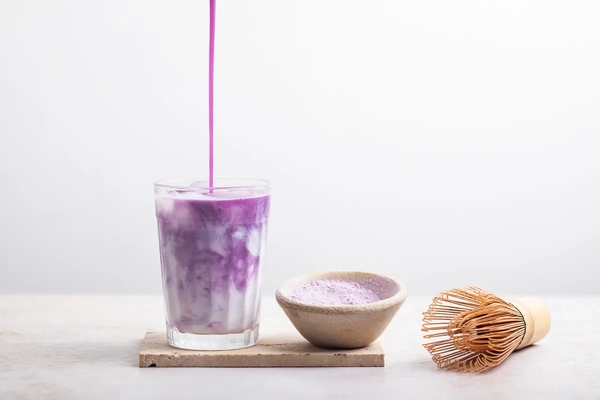 ube flavored syrup and milk pouring ube flavored syrup into glass of milk