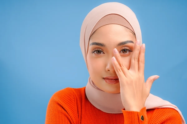 A girl in a hijab posing with her hand in front of her face.