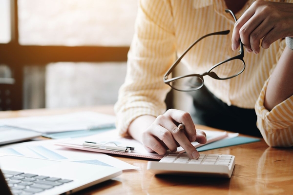 Image person uses calculator, holding glasses in hand
