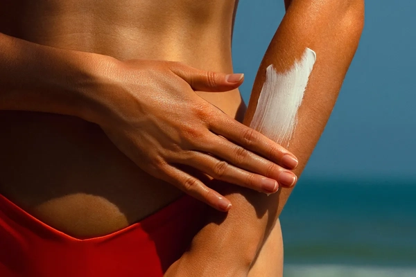 Image Woman applying sun screen to her arm on the beach