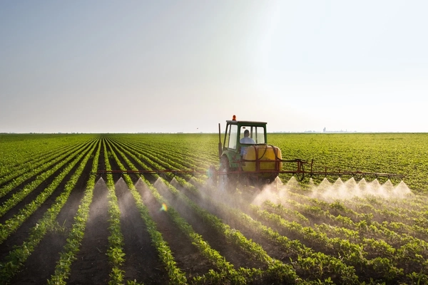 Image Farmer using a tractor to spray pesticides onto a field of crops.