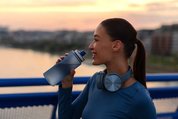 woman drinking water from a bottle outside while exercising