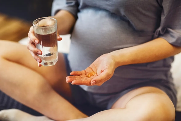Image Pregnant woman taking prenatal vitamins during pregnancy, holding water glass and pill in her hands