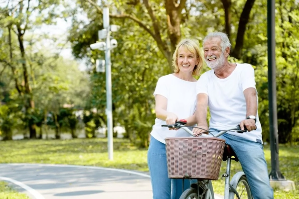 An older couple hanging out and the man is about to ride a bike with a pretty nice wicker basket on it.