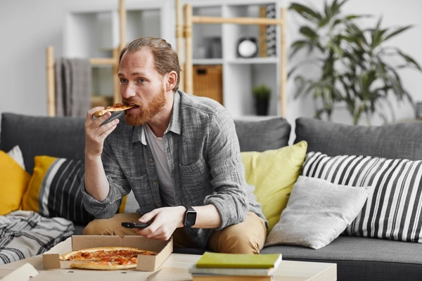 Image Man eating pizza alone on the sofa.