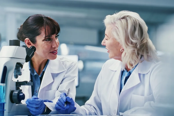 Image two women scientists having a discussion in lab with microscope,