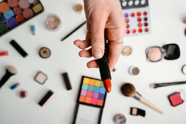 Image A woman's hand holding lipstick with other makeup in the background.